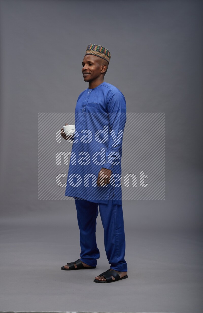 Man wearing Nigerian outfit standing holding mug on gray background