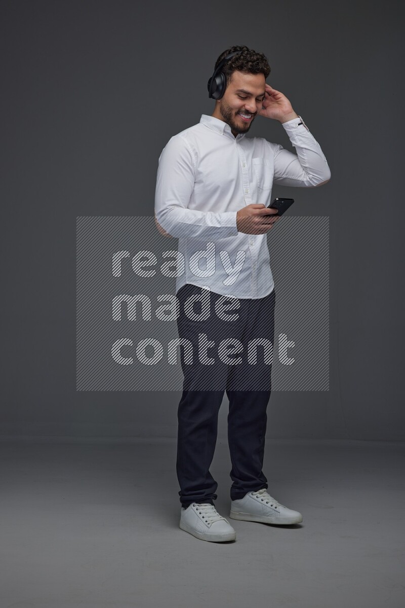 A man wearing smart casual and using his phone and headphone eye level on a gray background