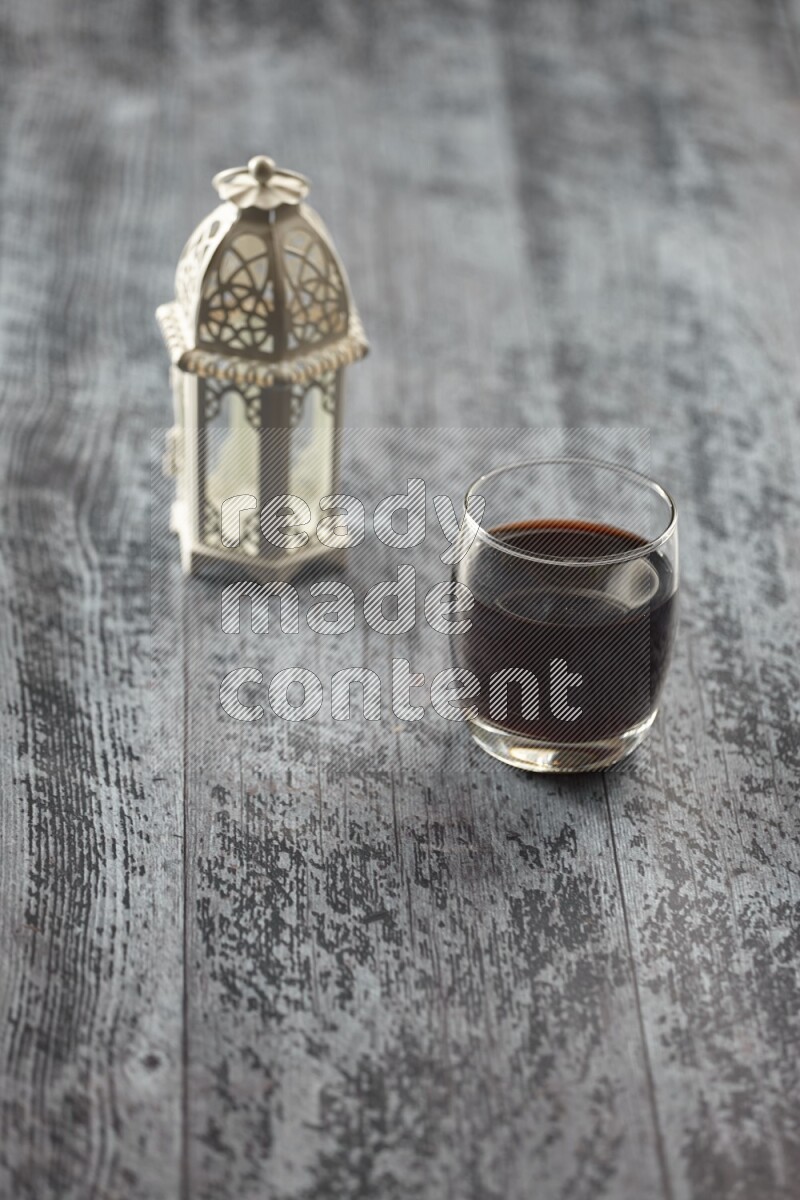 A white lantern with different drinks, dates, nuts, prayer beads and quran on grey wooden background
