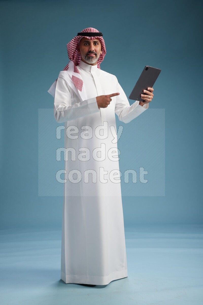 Saudi man wearing thob and shomagh with tablet on Blue background