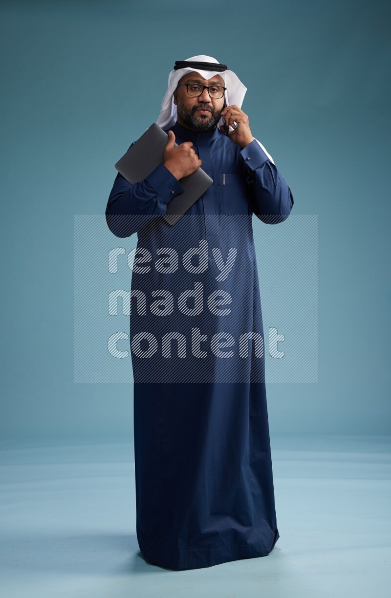 Saudi Man with shimag Standing talking on phone on blue background