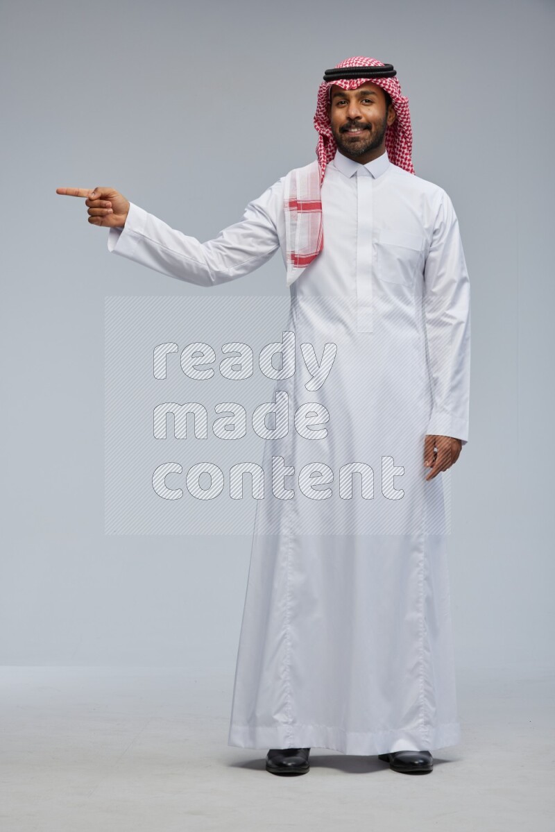 Saudi man Wearing Thob and shomag standing interacting with the camera on Gray background