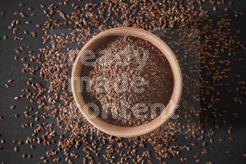 A wooden bowl full of flax surrounded by the seeds on a black flooring in different angles