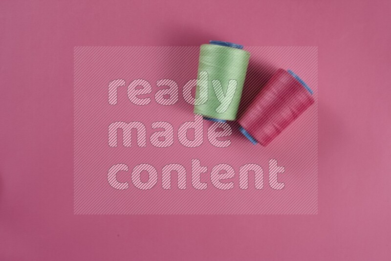 A green and pink collection of sewing and tailoring tools arranged on a pink background