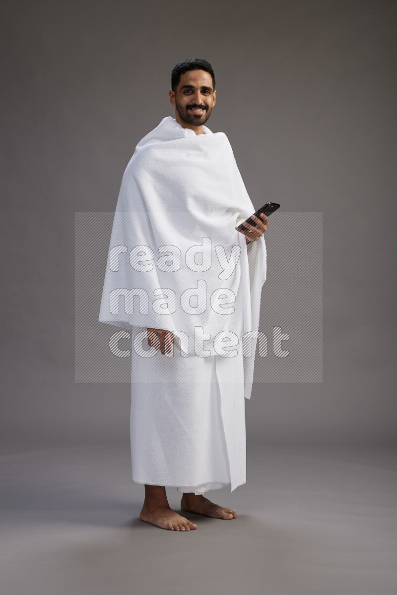 A man wearing Ehram Standing texting on phone on gray background