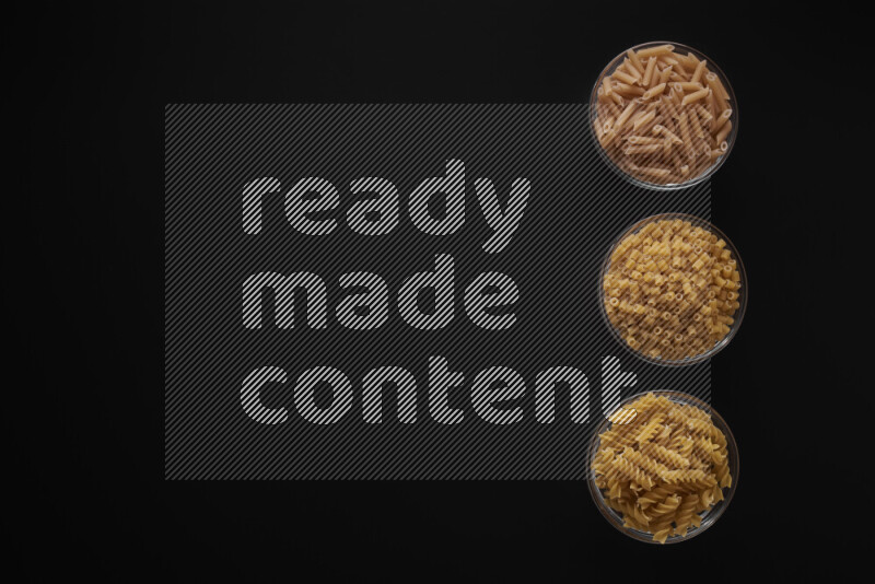 Different pasta types in 3 glass bowls on black background
