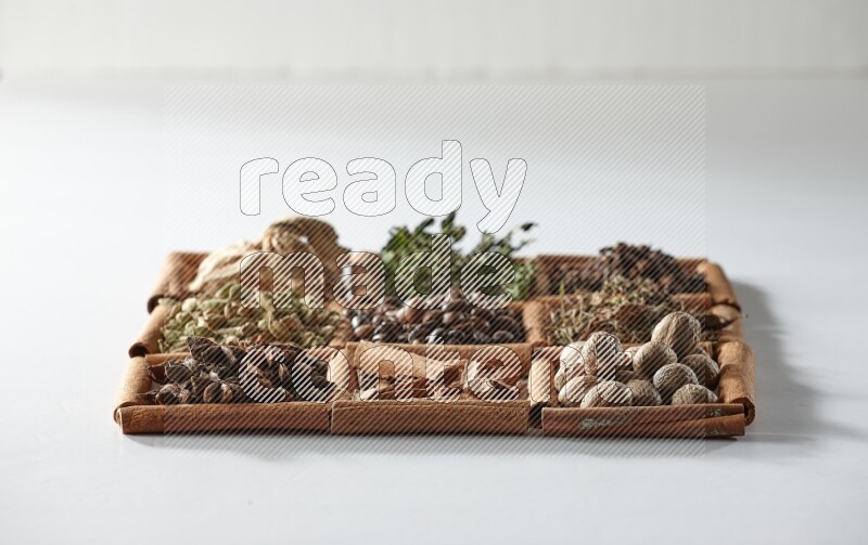 9 squares of cinnamon sticks full of coffee beans in the middle surrounded by dried mint, dried ginger, cardamom, star anise, cinnamon, nutmeg, dried basil and cloves on white flooring