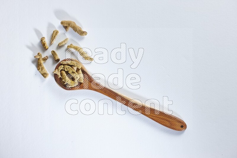 A wooden ladle full of dried turmeric fingers on white flooring
