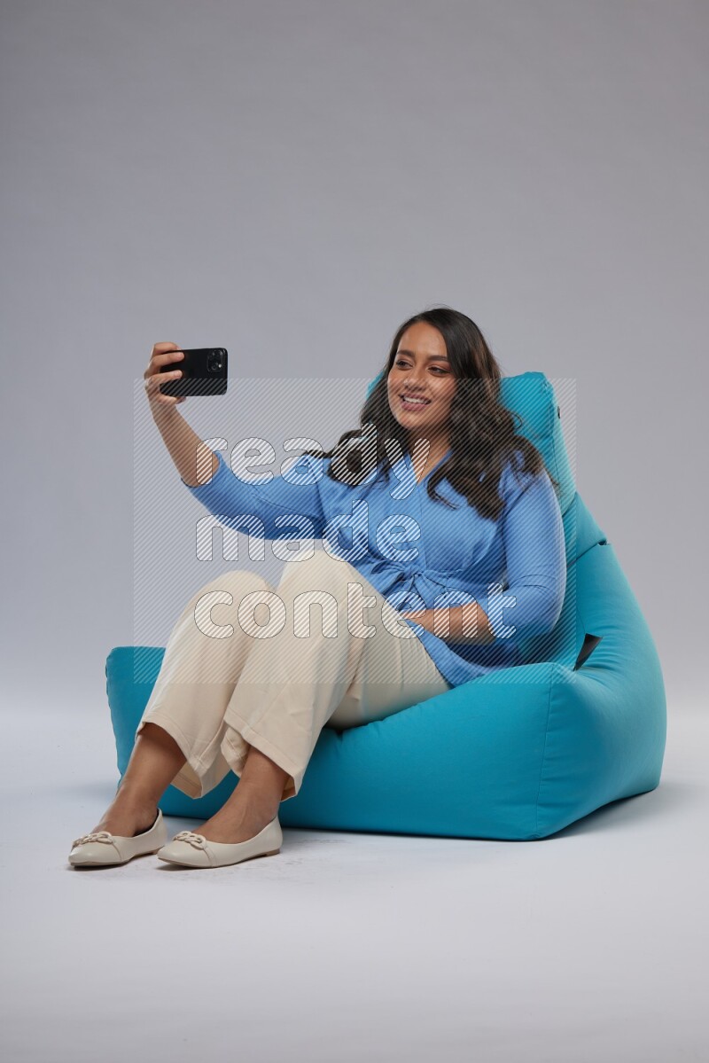 A woman sitting on a blue beanbag and taking selfie