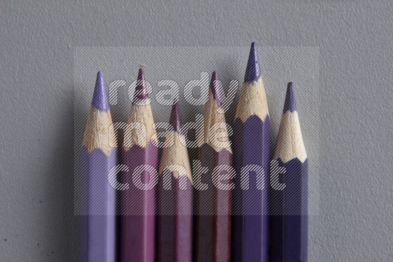 A collection of colored pencils arranged showcasing a gradient of purple hues on grey background