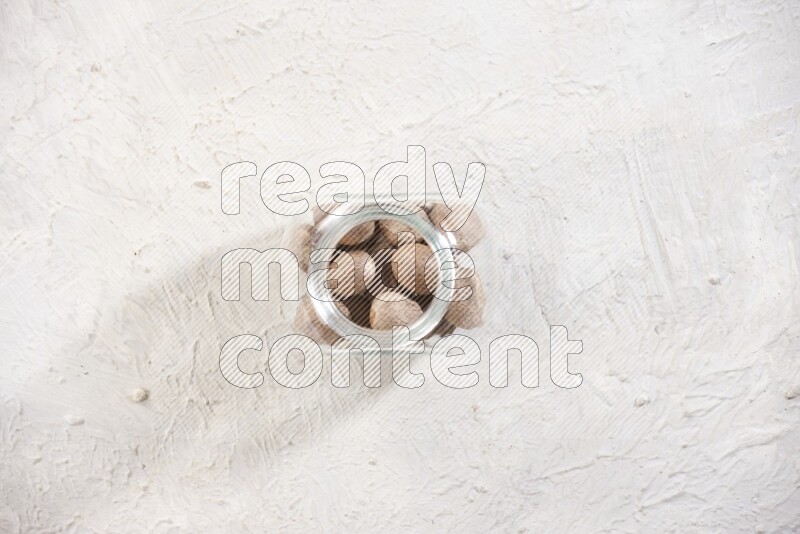 A glass spice jar full of whole nutmeg seeds on a textured white flooring