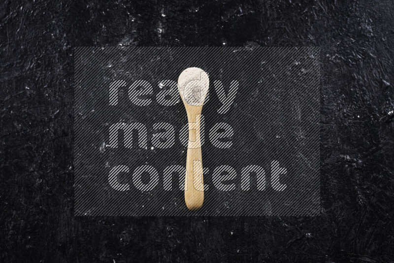A wooden spoon full of onion powder on black background