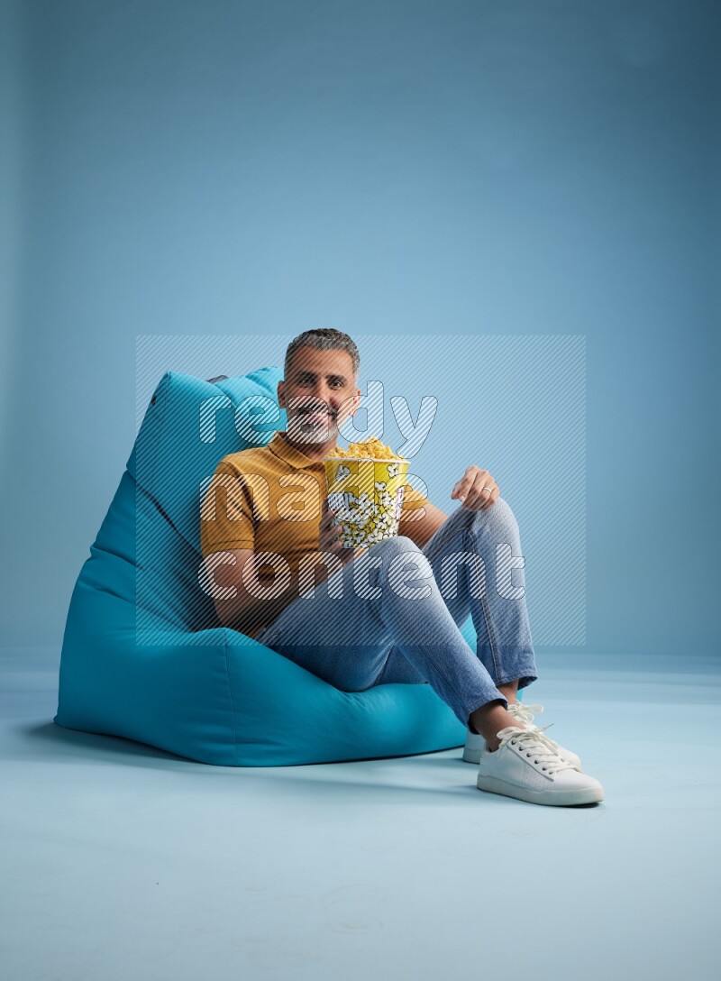A man sitting on a blue beanbag and eating popcorn