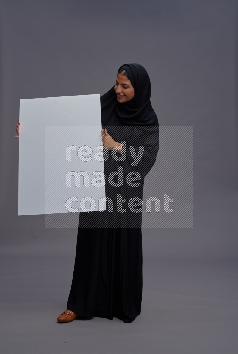 Saudi woman wearing Abaya standing holding white board on gray background