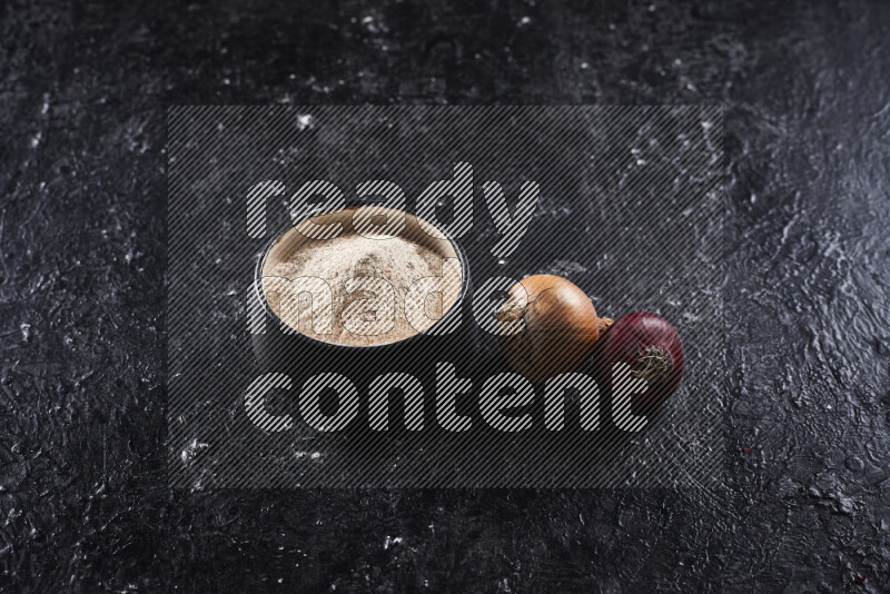 A black pottery bowl full of onion powder on black background