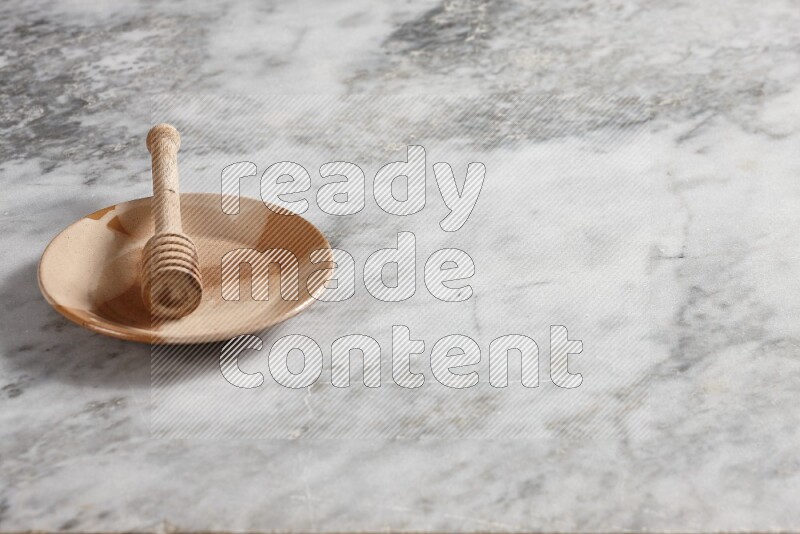 Multicolored pottery plate with wooden honey dipper in it on grey marble background