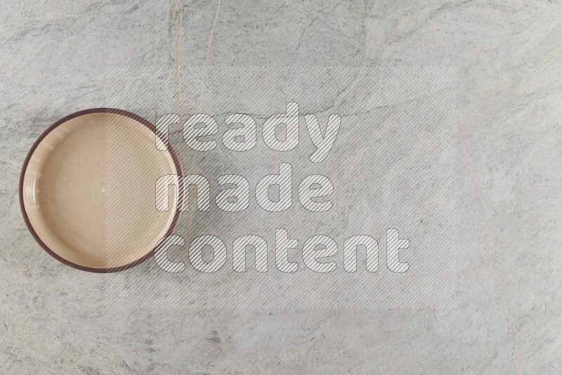 A beige pottery oven bowl on grey marble background