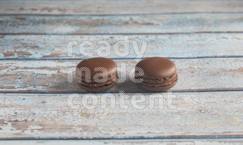 45º Shot of two Brown Dark Chocolate macarons on light blue wooden background