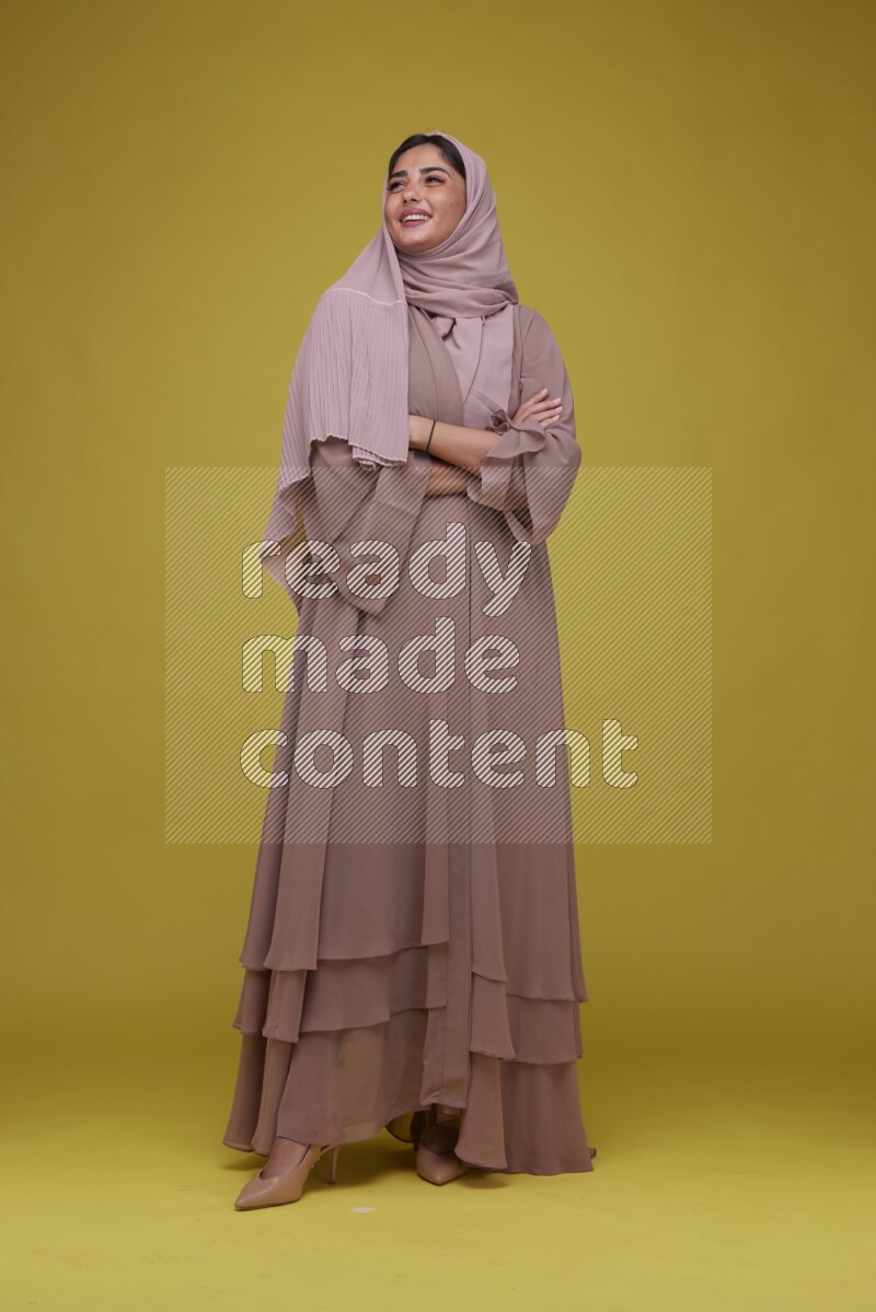 A woman Posing on a Yellow Background wearing Brown Abaya with Hijab