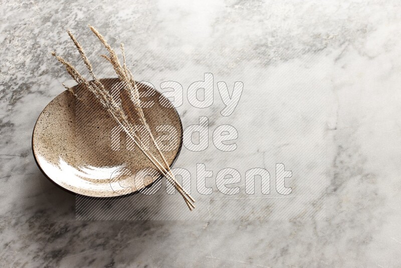 Wheat stalks on multicolored pottery plate on grey marble background