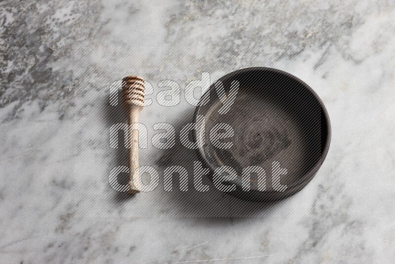 Black pottery oven plate with wooden honey dipper on the side on grey marble background