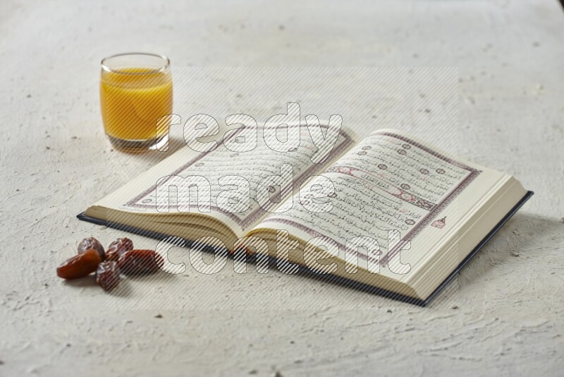 Quran with dates, prayer beads and different drinks all placed on textured white background