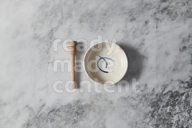 Multicolored pottery bowl with wooden honey dipper on the side on grey marble background