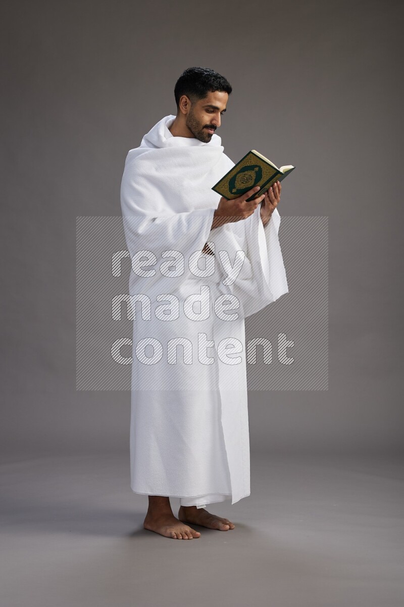 A man wearing Ehram Standing reading quran on gray background