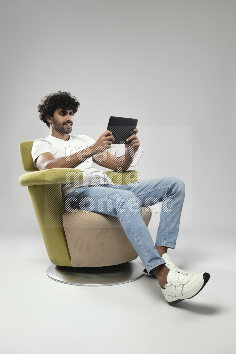 A man wearing casual sitting on a chair gaming on a tablet on white background