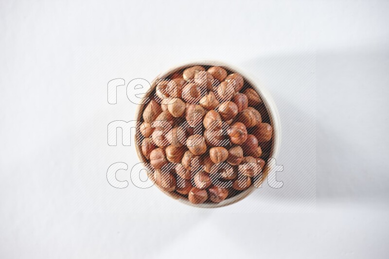 A beige ceramic bowl full of peeled hazelnuts on a white background in different angles
