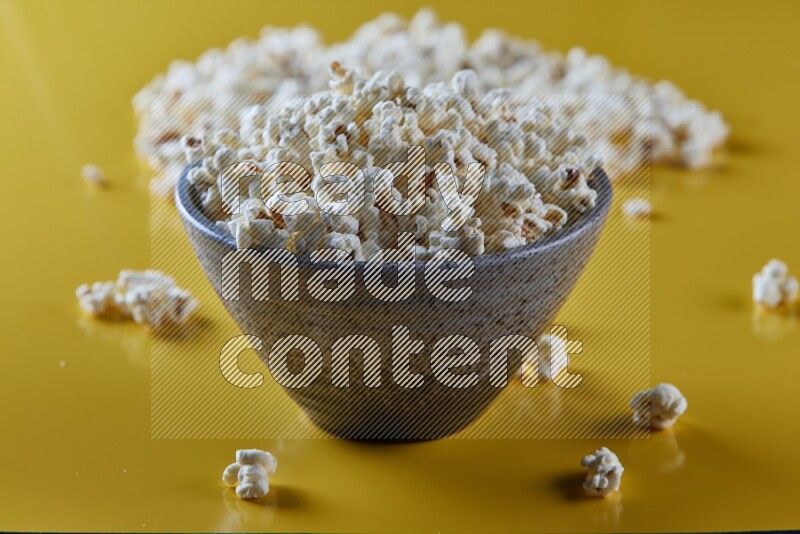 A multicolored pottery bowl full of popcorn with popcorn beside it on a yellow background in different angles