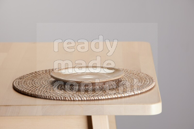 multi-colored pottery Plate placed on a big light colored straw placemat on the edge of wooden table