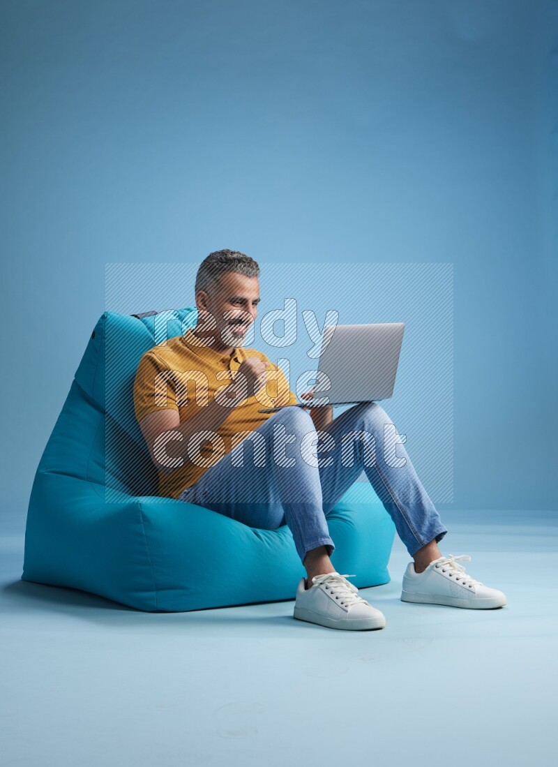 A man sitting on a blue beanbag and working on laptop