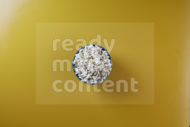 A blue pottery bowl full of popcorn on a yellow background in different angles