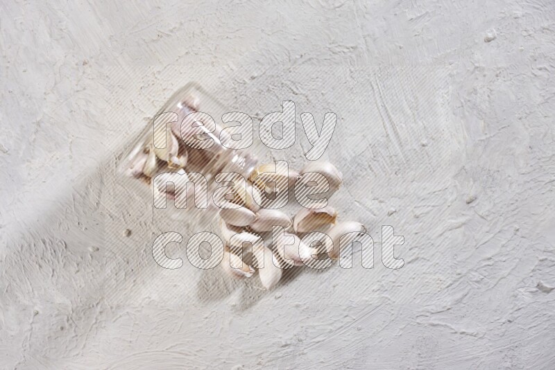 A glass jar full of garlic cloves flipped and the cloves came out on a textured white flooring