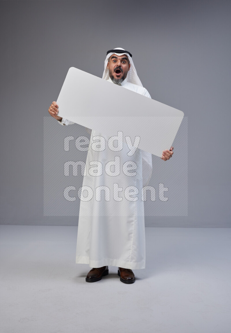 Saudi man Wearing Thob and white Shomag standing holding board on Gray background