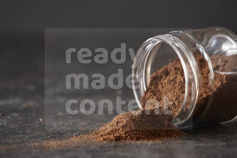 A flipped glass jar full of cloves powder on a textured black flooring