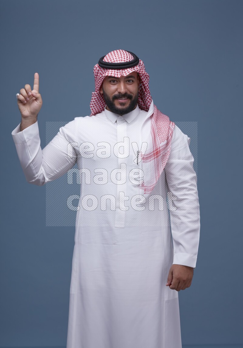 A man pointing on blue background wearing Saudi Thob with Shomag