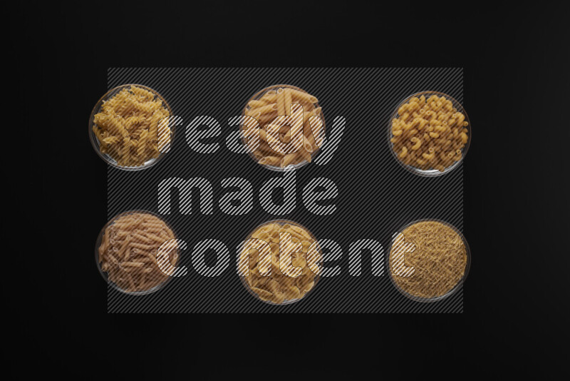 Different pasta types in 6 glass bowls on black background