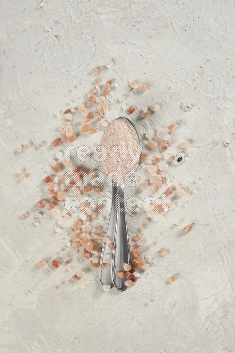 2 metal spoons filled with fine table salt and fine pink himalayan salt on white background