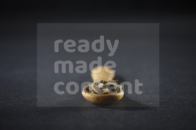 ملعقة خشبية ممتلئة بالهيل على خلفية سوداء