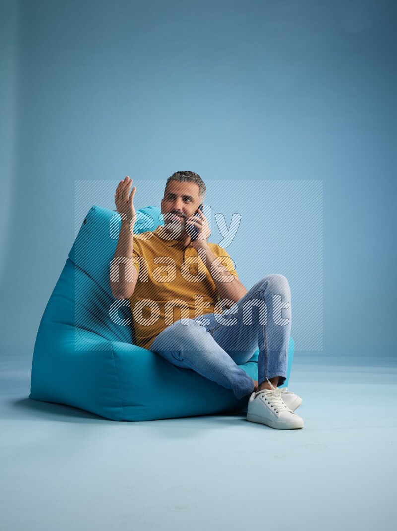 A man sitting on a blue beanbag and talking on the phone