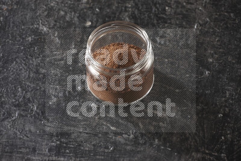 A glass jar full of cloves powder on a textured black flooring
