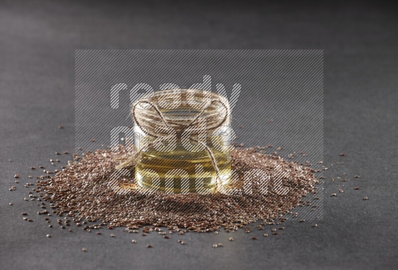 A glass jar full of flaxseeds oil surrounded by the seeds on a black flooring