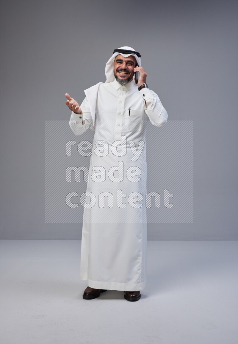 Saudi man Wearing Thob and white Shomag standing talking on phone on Gray background