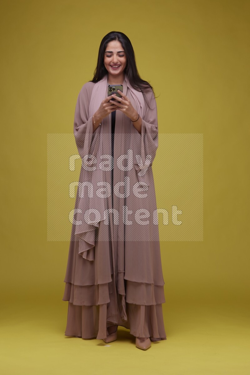 A woman Texting on a Yellow Background wearing Brown Abaya