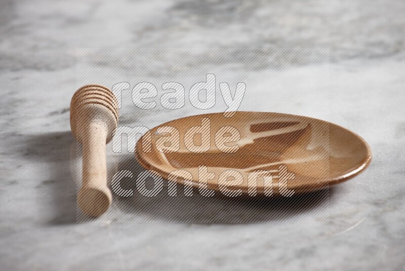 Multicolored pottery plate with wooden honey dipper on the side on grey marble background