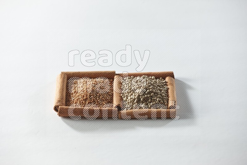 مربعان من أعواد القرفة ممتلئان بحبوب الخردل وحبوب الفلفل الأبيض علي خلفية بيضاء