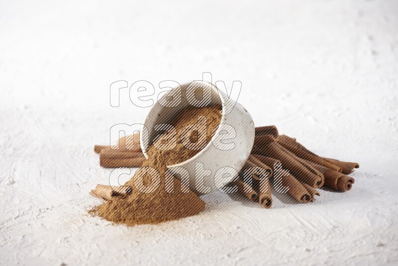 Ceramic beige bowl over filled with cinnamon powder and cinnamon sticks around the bowl on a textured white background in different angles