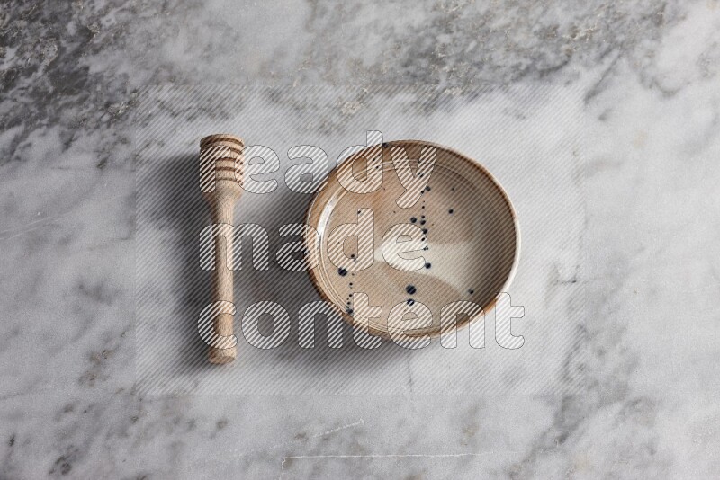 Multicolored pottery bowl with wooden honey dipper on the side on grey marble background